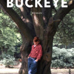 Cover von Buckeye von Patrick Ryan: Ein Junge in rotem Karohemd und blauen Jeans lehnt vor einem großen Baum, Parkkulisse.