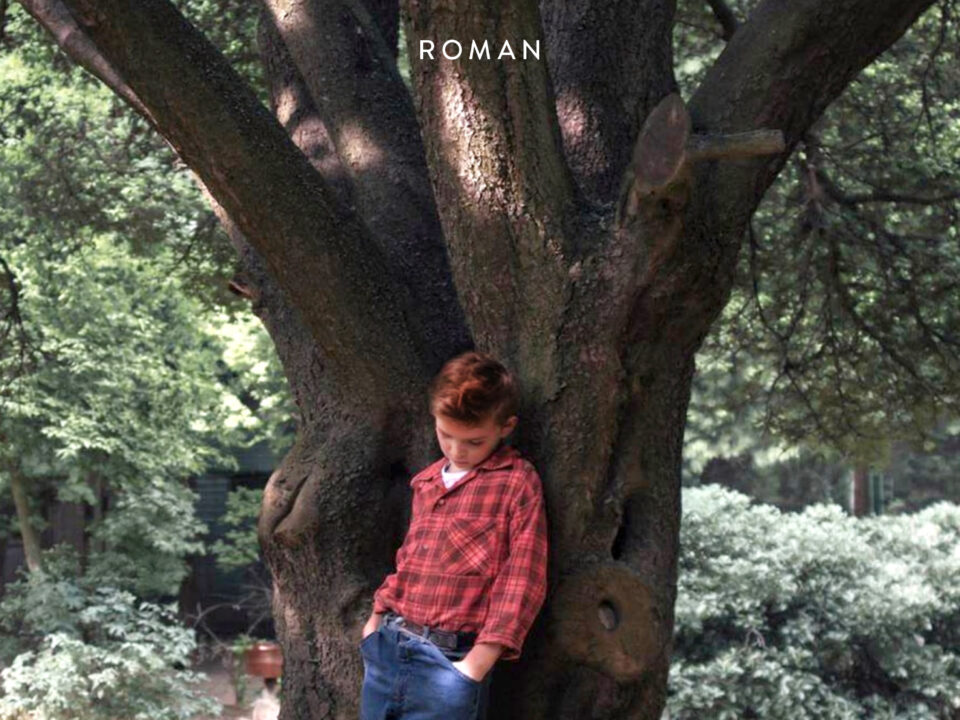 Cover von Buckeye von Patrick Ryan: Ein Junge in rotem Karohemd und blauen Jeans lehnt vor einem großen Baum, Parkkulisse.